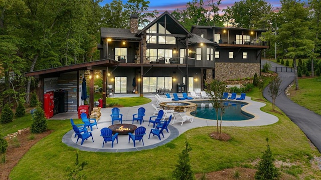 back house at dusk with a yard, a balcony, a patio, and an outdoor fire pit