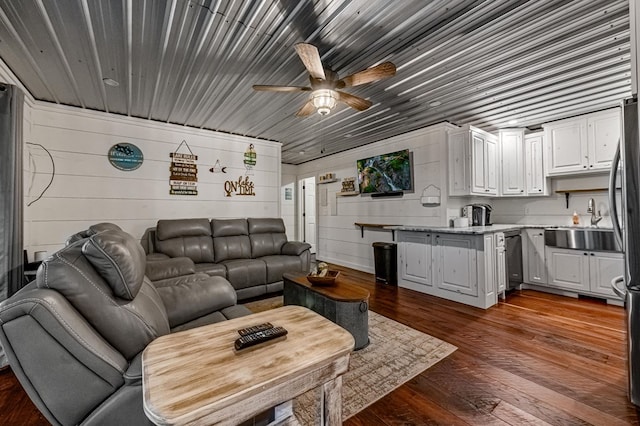 living room featuring wooden walls, dark hardwood / wood-style flooring, ceiling fan, and sink