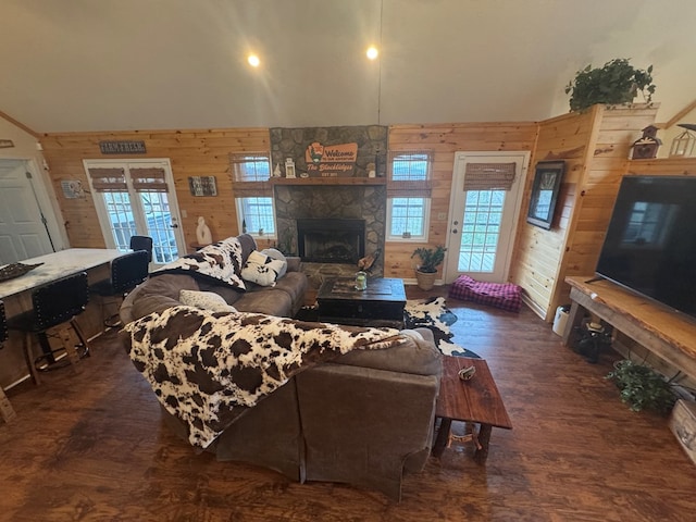 living room featuring wooden walls, vaulted ceiling, wood finished floors, and a stone fireplace