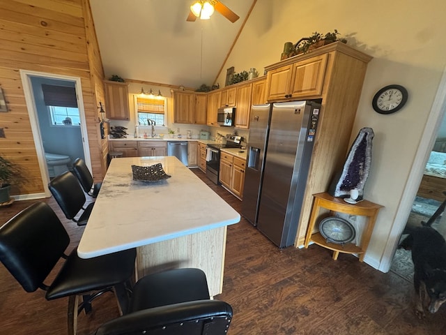 kitchen with a ceiling fan, appliances with stainless steel finishes, dark wood-style flooring, a center island, and light countertops