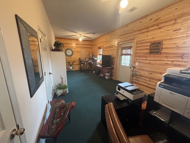 office area featuring carpet floors, visible vents, ceiling fan, wooden walls, and a textured ceiling