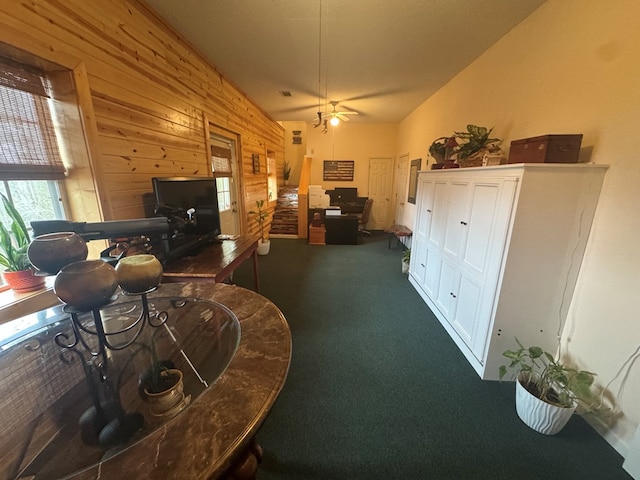 carpeted living area with lofted ceiling, wood walls, and a ceiling fan