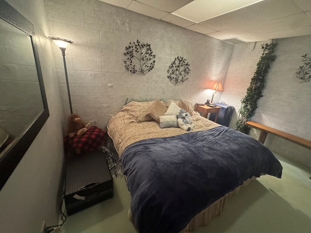 bedroom with concrete block wall, a paneled ceiling, and concrete flooring