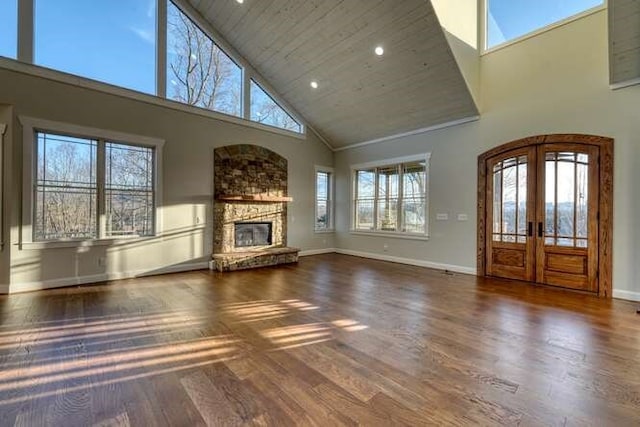 unfurnished living room with wood ceiling, a towering ceiling, dark hardwood / wood-style flooring, a stone fireplace, and french doors