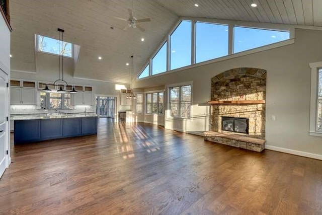 unfurnished living room with a high ceiling, a stone fireplace, and dark wood-type flooring