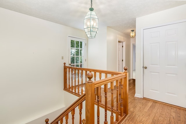 hallway featuring a textured ceiling, light hardwood / wood-style flooring, and a notable chandelier