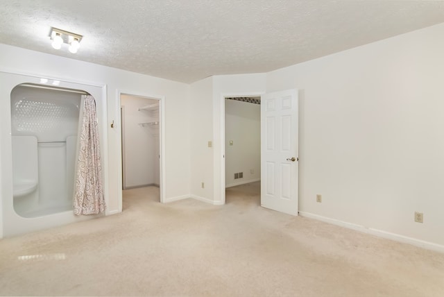 unfurnished bedroom featuring a closet, a spacious closet, light carpet, and a textured ceiling