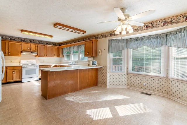 kitchen with ceiling fan, white gas stove, kitchen peninsula, and a textured ceiling