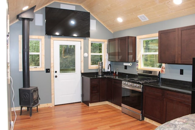 kitchen featuring a wood stove, stainless steel range with gas stovetop, vaulted ceiling, a sink, and dark stone counters