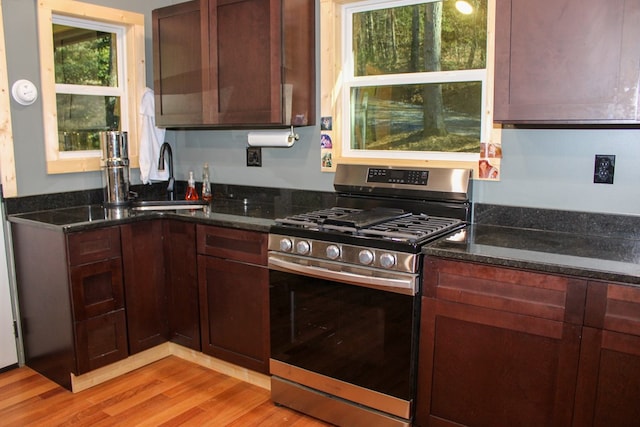 kitchen with dark stone counters, light wood-style flooring, a sink, and stainless steel range with gas stovetop