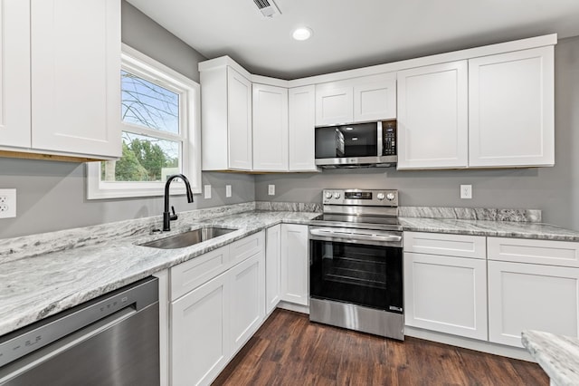 kitchen with sink, appliances with stainless steel finishes, white cabinetry, light stone countertops, and dark hardwood / wood-style flooring