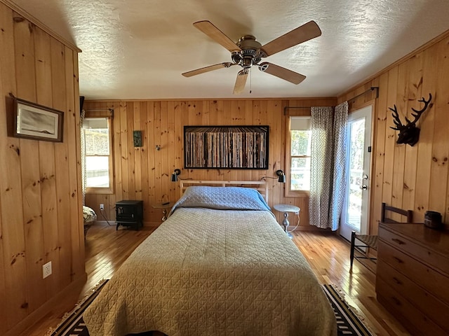 bedroom with light hardwood / wood-style floors, multiple windows, wooden walls, and ceiling fan