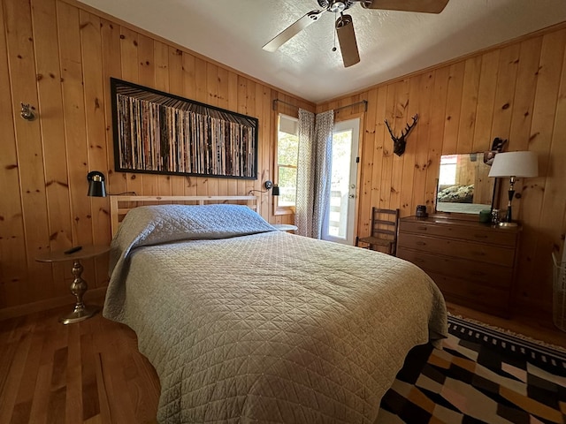 bedroom featuring wooden walls, hardwood / wood-style flooring, a textured ceiling, and ceiling fan