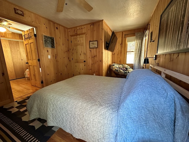 bedroom with wood finished floors, a textured ceiling, wood walls, and a ceiling fan