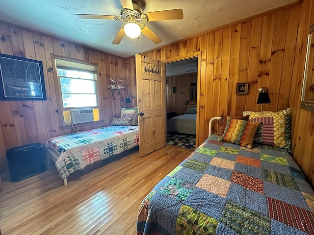 bedroom featuring ceiling fan, wood walls, cooling unit, and light wood finished floors