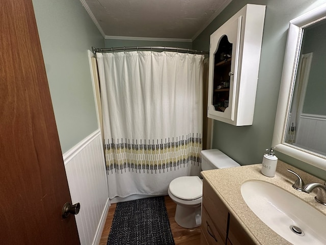 bathroom featuring wood finished floors, toilet, vanity, ornamental molding, and wainscoting