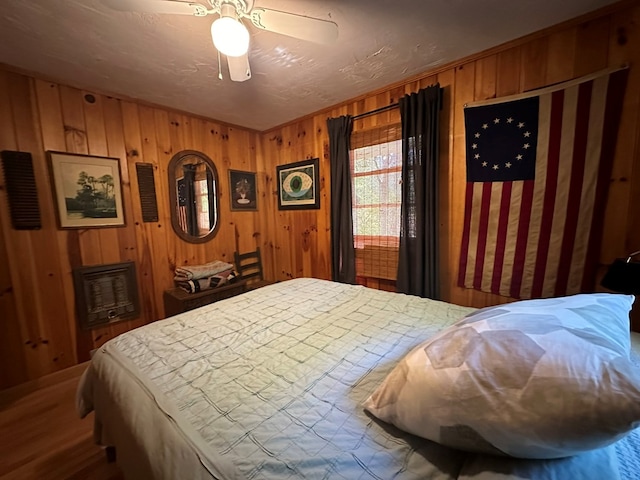 bedroom with wood walls, a ceiling fan, and wood finished floors