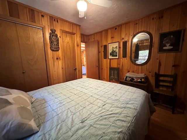 bedroom featuring wooden walls, wood finished floors, a closet, and a ceiling fan
