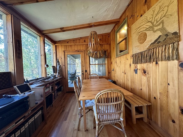 dining area featuring wood finished floors, wood walls, and beam ceiling