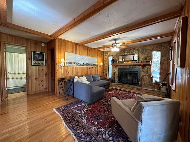 living room featuring beam ceiling, wooden walls, a stone fireplace, and light hardwood / wood-style floors