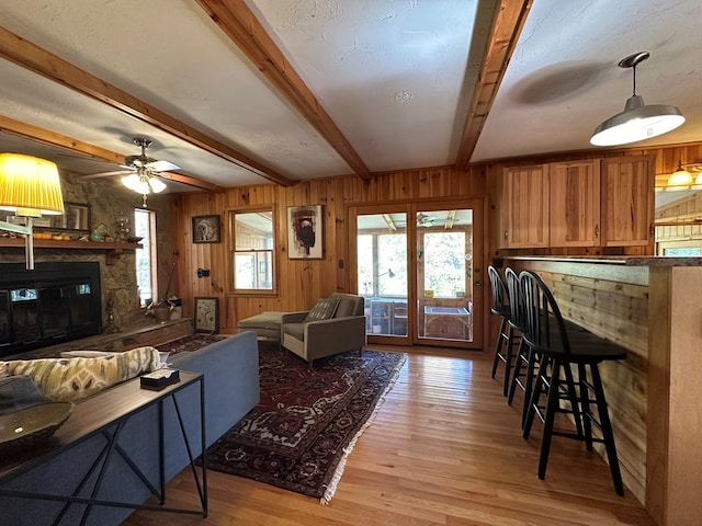 living area with light wood-style flooring, ceiling fan, a fireplace, wood walls, and beam ceiling