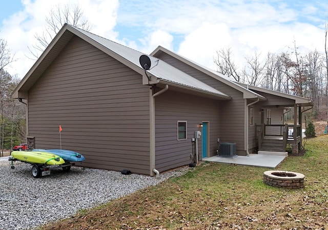 view of home's exterior with metal roof, central AC, an outdoor fire pit, and driveway