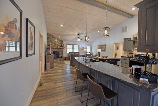 kitchen featuring a breakfast bar, a sink, visible vents, dark wood-style floors, and gas stove