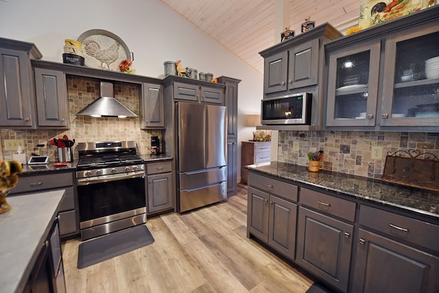 kitchen featuring stainless steel appliances, light wood-type flooring, vaulted ceiling, and wall chimney exhaust hood