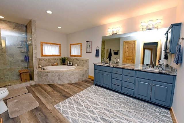 bathroom featuring a garden tub, double vanity, a tile shower, a sink, and wood finished floors