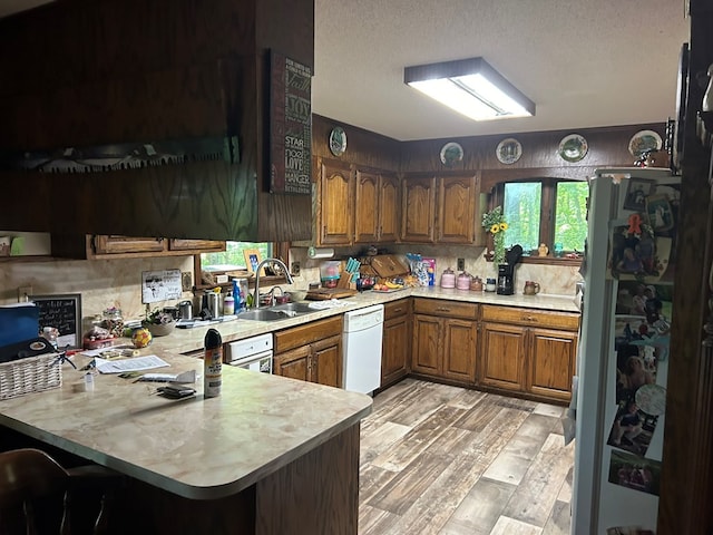 kitchen featuring brown cabinets, a sink, white appliances, a peninsula, and light countertops