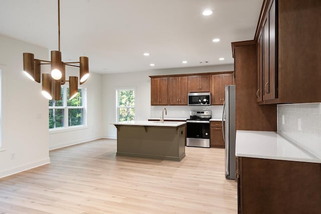 kitchen featuring an island with sink, light wood-type flooring, appliances with stainless steel finishes, and pendant lighting