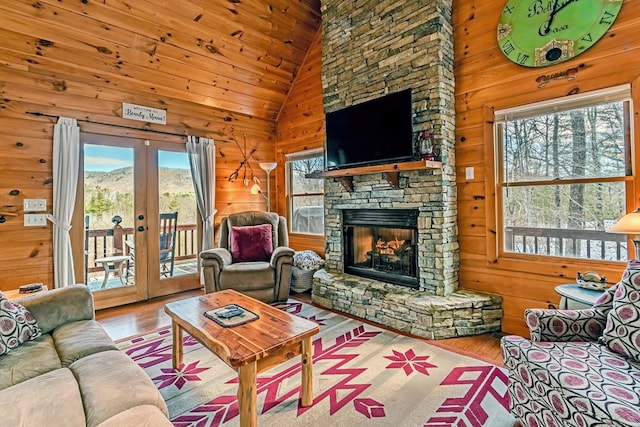 living room with light wood-style floors, wooden walls, a stone fireplace, and french doors