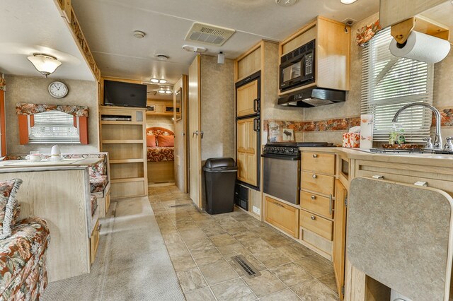 kitchen with black microwave, stainless steel range oven, sink, and light brown cabinetry