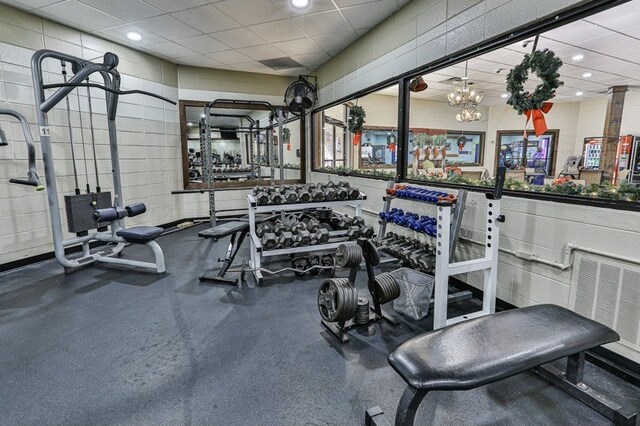 workout area with a paneled ceiling and a chandelier