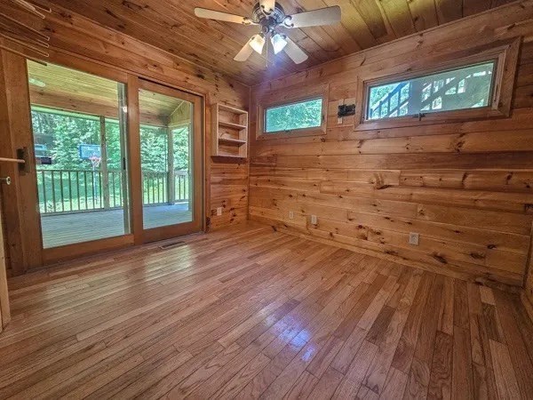 unfurnished room featuring wood ceiling, ceiling fan, a healthy amount of sunlight, hardwood / wood-style flooring, and wood walls