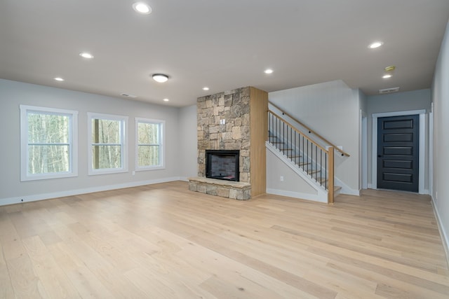 unfurnished living room featuring stairway, baseboards, a fireplace, and light wood-type flooring