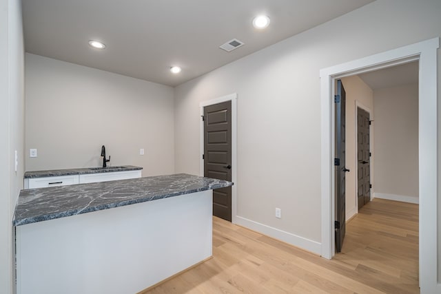 kitchen featuring visible vents, a sink, baseboards, dark stone countertops, and light wood-style flooring