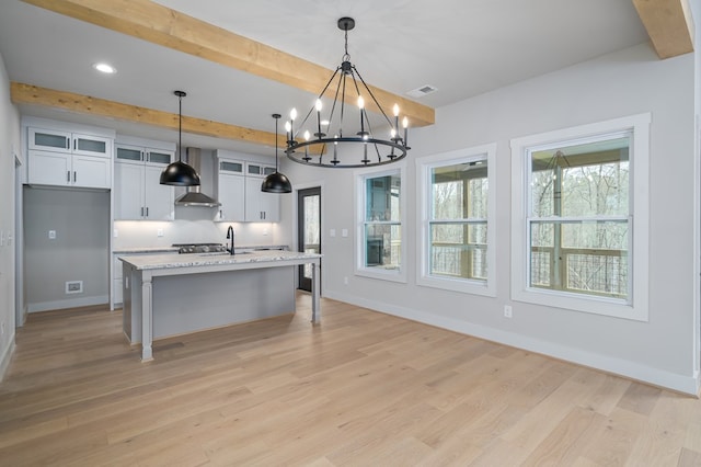 kitchen featuring wall chimney range hood, visible vents, a sink, a notable chandelier, and white cabinetry