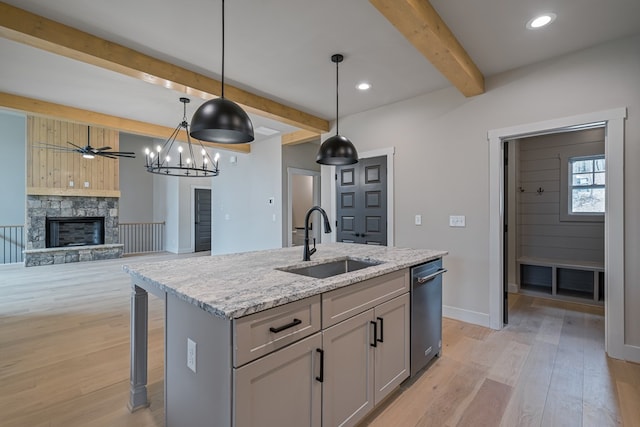 kitchen with a sink, baseboards, light wood-type flooring, stainless steel dishwasher, and beamed ceiling