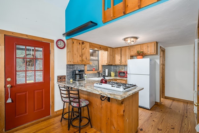 kitchen with white appliances, tasteful backsplash, sink, light wood-type flooring, and kitchen peninsula