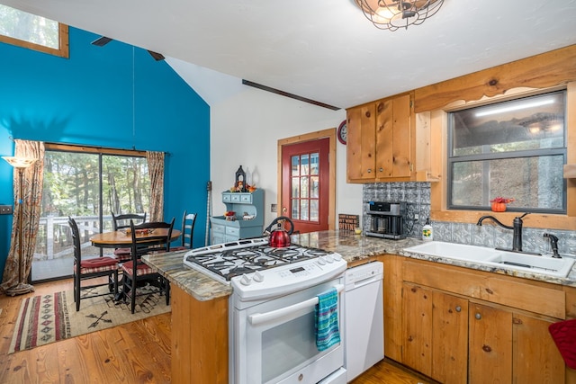 kitchen with white appliances, sink, kitchen peninsula, light stone counters, and light hardwood / wood-style flooring