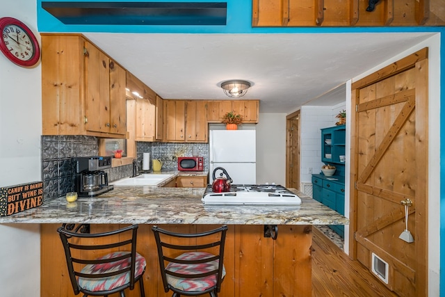 kitchen with kitchen peninsula, tasteful backsplash, a breakfast bar area, sink, and white appliances