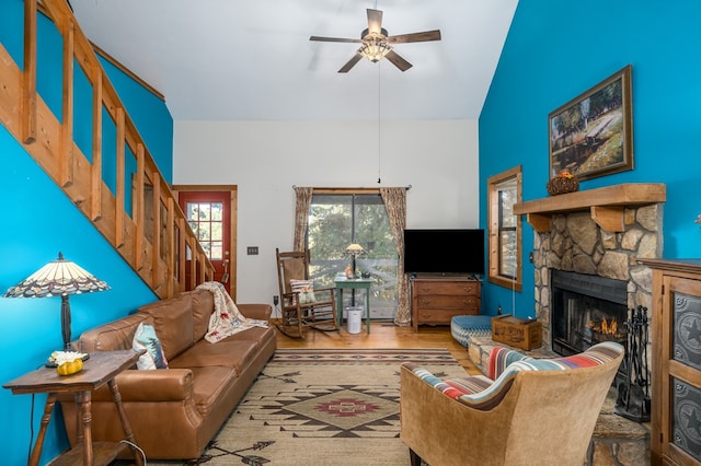 living room featuring lofted ceiling, light hardwood / wood-style flooring, a stone fireplace, and ceiling fan