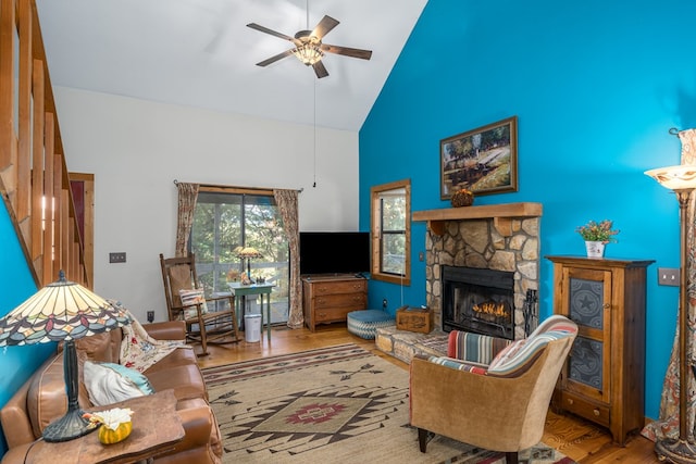 living room featuring a stone fireplace, high vaulted ceiling, light wood-type flooring, and ceiling fan