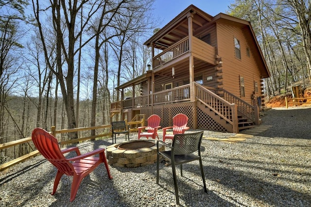 back of property with stairway, a fire pit, a wooden deck, log siding, and a balcony