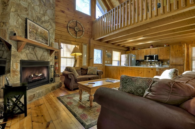 living area featuring a stone fireplace, wooden walls, a healthy amount of sunlight, and light wood finished floors