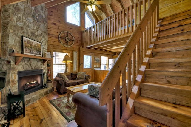 living room with hardwood / wood-style floors, a healthy amount of sunlight, a stone fireplace, stairs, and wood walls