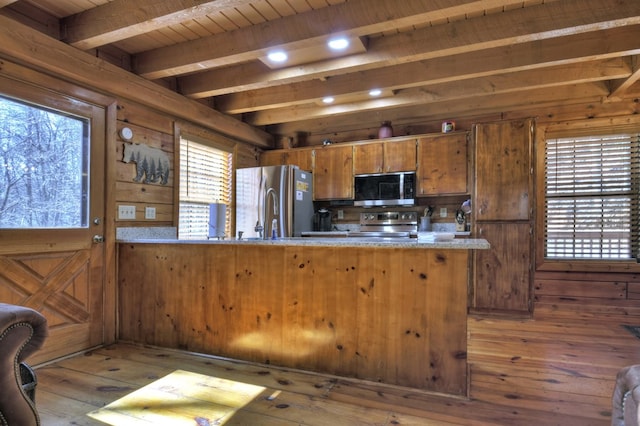 kitchen featuring beamed ceiling, brown cabinets, appliances with stainless steel finishes, a peninsula, and light countertops