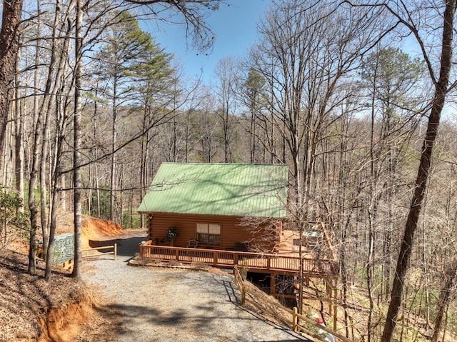 exterior space featuring driveway, a deck, log exterior, a view of trees, and metal roof