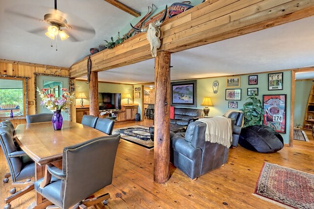 dining area featuring wood-type flooring, wood walls, ceiling fan, and beamed ceiling